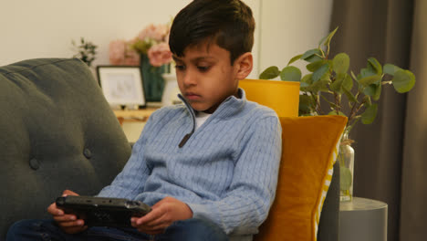 Young-Boy-Sitting-On-Sofa-At-Home-Playing-Game-Or-Streaming-Onto-Handheld-Gaming-Device-1